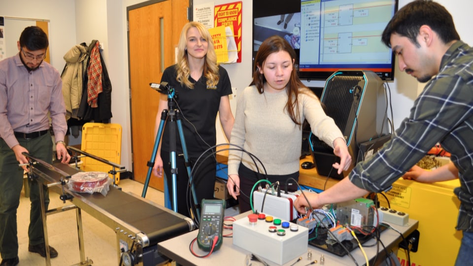 Santiago Guevara, Brittany Newell, Laura Vallejo and Jose Chamorro work with a conveyor belt test system and sensors in the Adaptive Additive Technologies Lab.