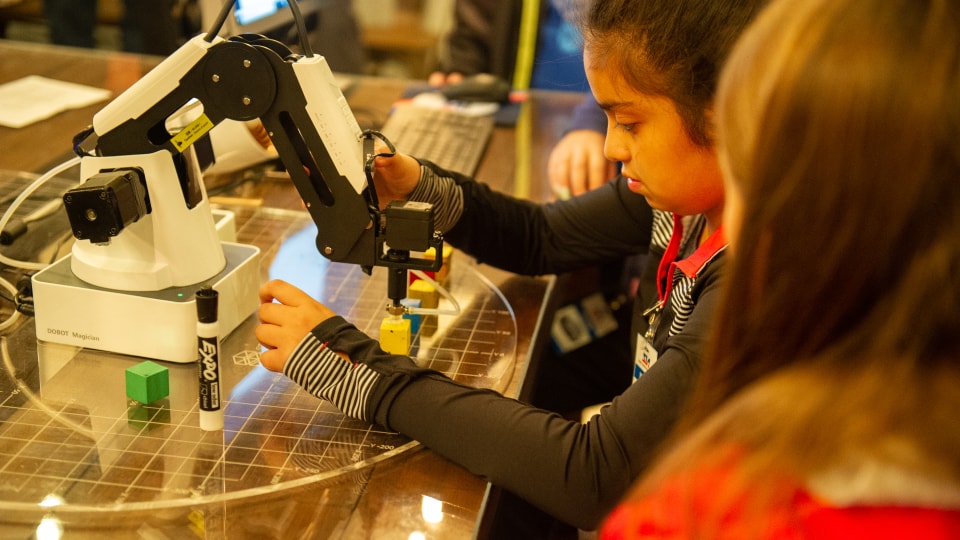 Elementary school students learn to execute tasks with a robotic arm much like those found in advanced manufacturing facilities.