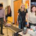Santiago Guevara, Brittany Newell and Laura Vallejo with a conveyor belt test system and sensors in the Adaptive Additive Technologies Lab.